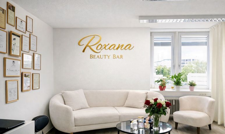 Wartebereich von Roxana Beauty Bar mit Sofa und goldenem Studio-Schriftzug